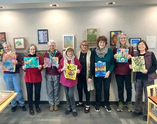 Eight women hold their artwork made in the Experimental Techniques in Watercolor and Gouache class.
